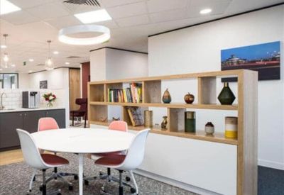 Bright communal breakout area with a round table, pink chairs, and a decorative bookshelf.