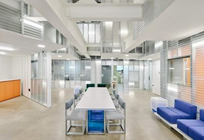 Open-plan work area with blue couches and a large conference table under a white industrial ceiling.