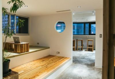 Bright coworking area with a laptop on a wooden stand and a circular porthole window.