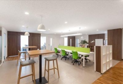 Spacious communal coworking area with high-top tables, green chairs, and wooden cabinetry.