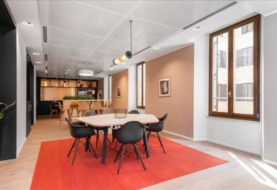 Contemporary breakout space with a round table, black chairs, and a vibrant red area rug.