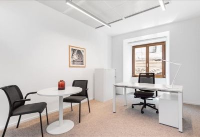 Bright private office suite featuring a white desk, ergonomic chair, and small round meeting table.