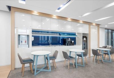 Communal break area with small round tables and a sleek white kitchenette.