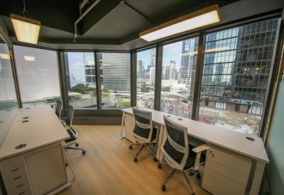 Corner office suite with multiple workstations and floor-to-ceiling windows showing city skyscrapers.