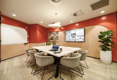 Modern meeting room with a white table, grey chairs, and a wall-mounted screen.