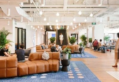 Wide view of a modern breakout area featuring leather sofas, blue rugs, and hanging globe lights.