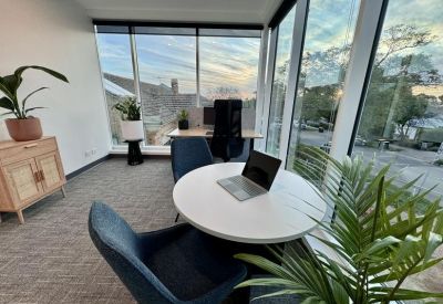 Corner meeting area with a round white table, blue chairs, and a desktop computer.