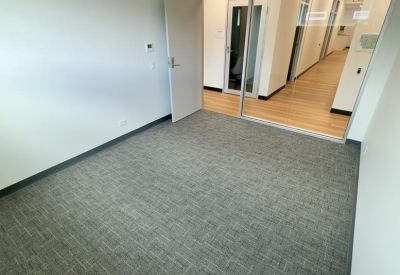 Empty office room with grey carpet and a glass wall looking into a hallway.
