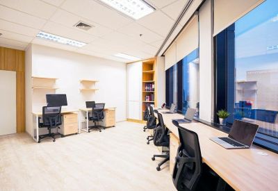 Bright office space with individual wooden desks and ergonomic chairs along a window wall.