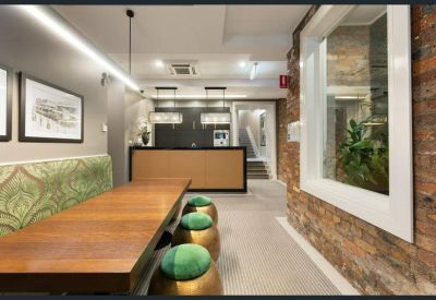 Dining area with a long timber table, green patterned bench seating, and exposed brick walls.