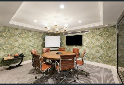 Circular meeting room with patterned green wallpaper, timber table, and tan leather chairs.
