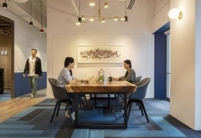 Meeting area with a heavy timber table and blue bucket chairs on a patterned rug.