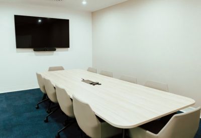 Minimalist conference room featuring a wall-mounted TV screen and grey carpeting.
