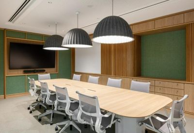 Large boardroom with a light wood table, grey mesh chairs, and green acoustic wall panels.