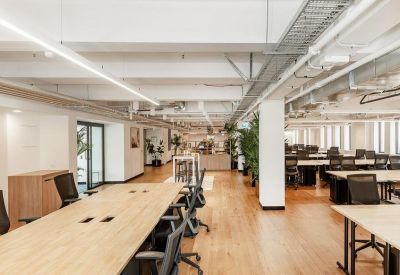 Bright open-plan office with wooden floors and exposed ceiling pipes.