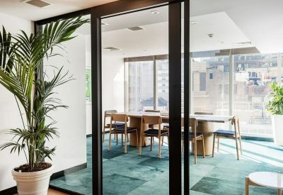 Modern glass-walled meeting room with a teal carpet and wooden table.