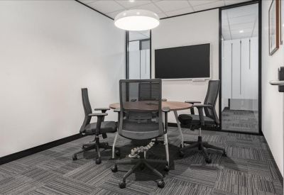 Professional meeting room with a round table, mesh chairs, and a wall-mounted screen.