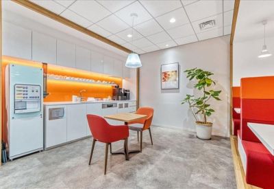 Communal kitchen and dining area with modern white cabinetry, red chairs, and a vibrant orange backsplash.