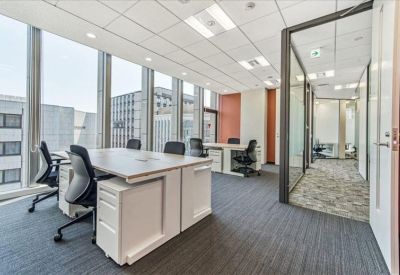 Spacious corner office with white desks, ergonomic chairs, and panoramic city views through floor-to-ceiling windows.