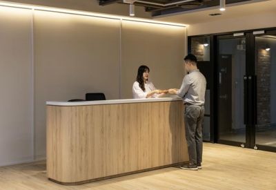 Sleek wooden reception desk with a staff member assisting a visitor.