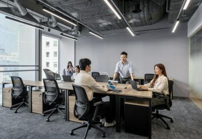 Spacious open-plan office with multiple workstations and a team member standing to discuss work.