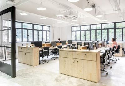Professional office floor with rows of desks, ergonomic chairs, and large industrial windows.