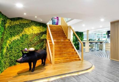 Stylish reception area with a green plant wall, wooden staircase, and black pig sculpture.