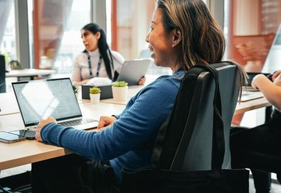 Coworker in a blue sweater sitting at a desk with a branded Melbourne Connect tote bag.