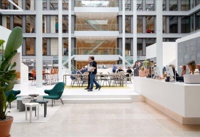 Sunlit multi-story atrium communal area with white desks and green lounge chairs.