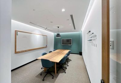 Bright conference room with a long wooden table, teal chairs, and a large whiteboard.