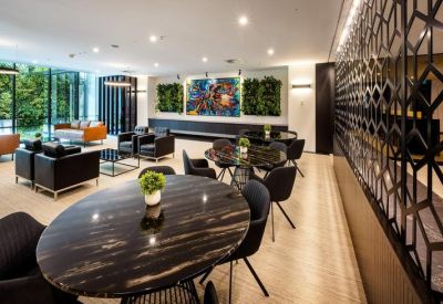 Bright communal lounge and dining area with marble tables and green plant walls.