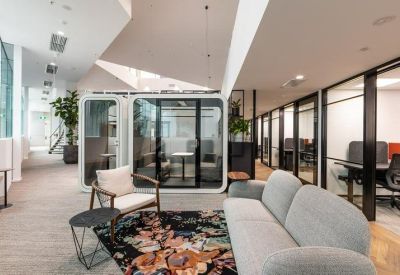 Lounge area with a grey sofa, floral rug, and glass-walled meeting pods.