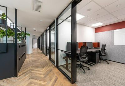 Hallway view of private glass-walled office suites and wooden herringbone flooring.