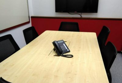 Meeting room with a light wood table, black chairs, and a wall-mounted TV.