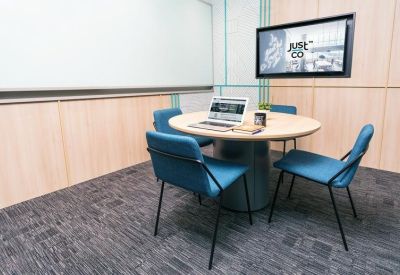 Four-person meeting room with blue chairs and a wall-mounted monitor.