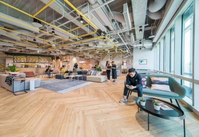 Wide-angle view of a bright coworking space with herringbone floors and industrial ceiling.