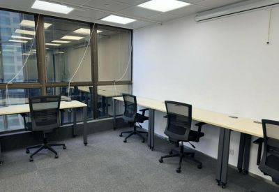 Bright office workspace with multiple desks, black rolling chairs, and large windows.
