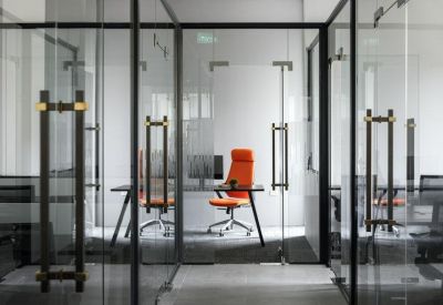 Modern private office with glass partitions and a vibrant orange ergonomic chair.
