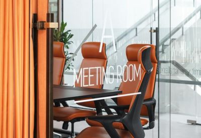 Glass-walled meeting room featuring orange leather chairs and a dark conference table.