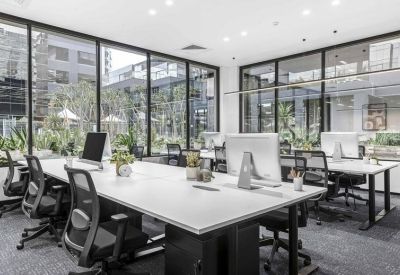 Bright open-plan office with white desks, ergonomic black chairs, and floor-to-ceiling windows.