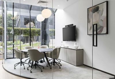 Sunlit meeting room with a round table, grey chairs, and a flat-screen TV.