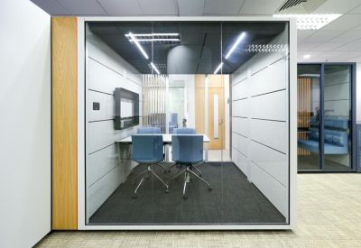 Private four-person glass meeting pod with blue chairs and acoustic wall panels.