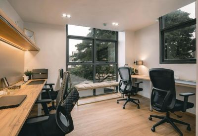Quiet private office space with wooden desks, ergonomic chairs, and a large window for natural light.