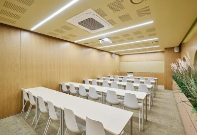 Bright meeting room with white chairs, long tables, and light wood paneled walls.