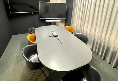 Modern meeting room with a grey oval table and dual wall-mounted monitors.
