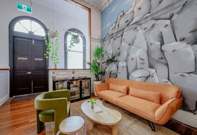Spacious reception lounge with a green velvet chair, orange sofa, and large stone-patterned feature wall.