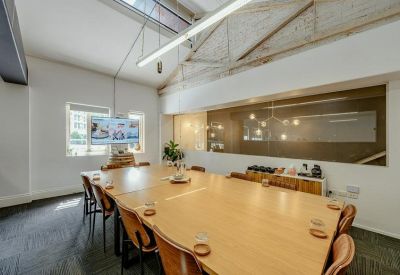 Modern meeting room with a large light-wood table, vaulted ceilings, and a wall-mounted screen.