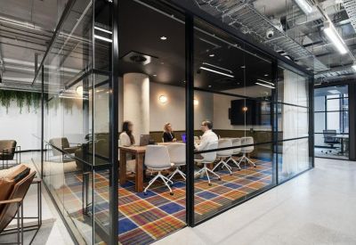 Glass-walled boardroom with a wooden table, white chairs, and colourful plaid carpet.