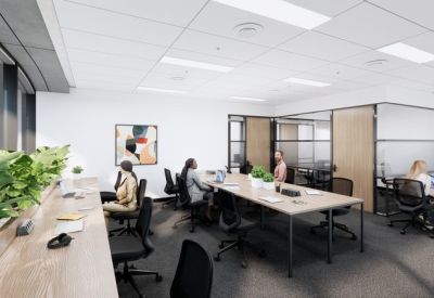 Bright open-plan office with communal desks, indoor plants, and large windows.
