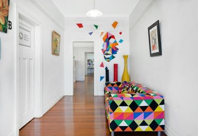 White hallway featuring vibrant geometric wall art and a matching colorful sofa.